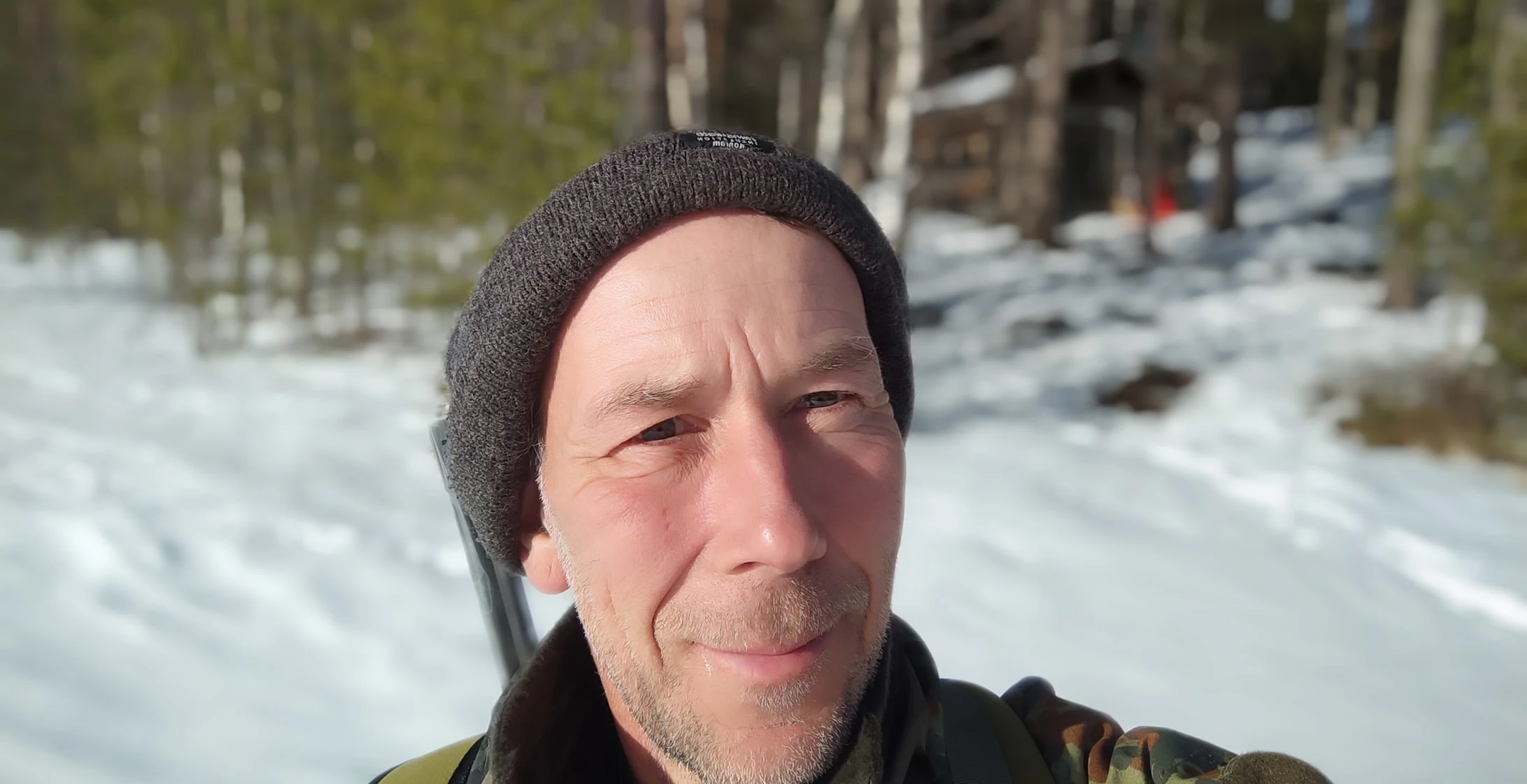 Wintertrekking mit Schneeschuhen, Pulka, Zelt und Ofen. Dirk mit Gewehr vor Hütte.